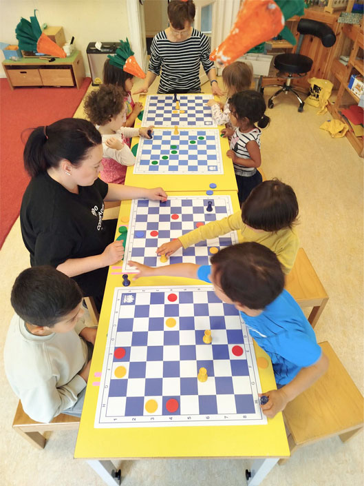 Kinder beim Schachspielen mit einer Erzieherin in der Kita