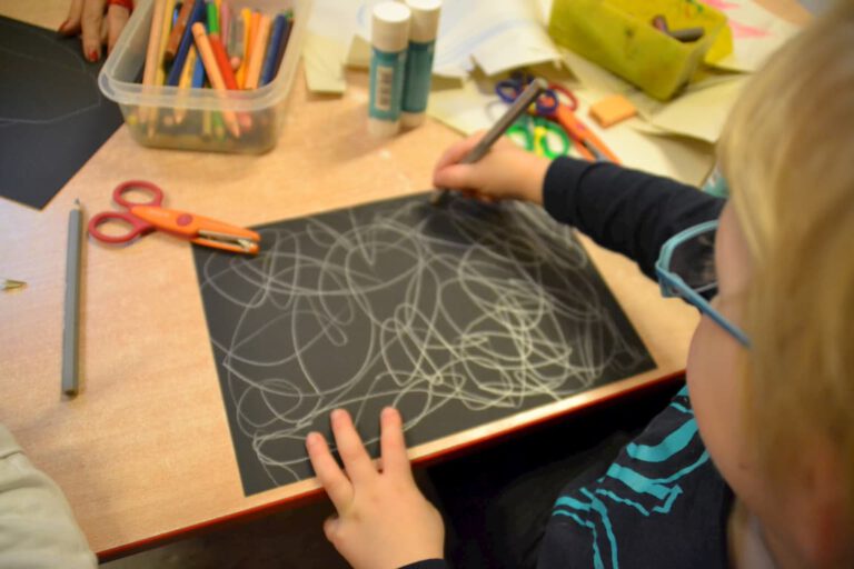 Kind malt mit Kreide auf schwarzem Papier in der Kita Moa